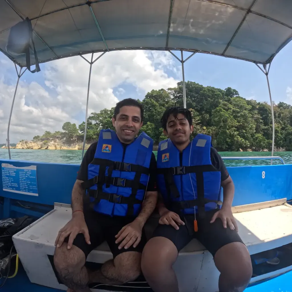 Couple in life jackets on the boat with an island behind, island hopping in Andaman