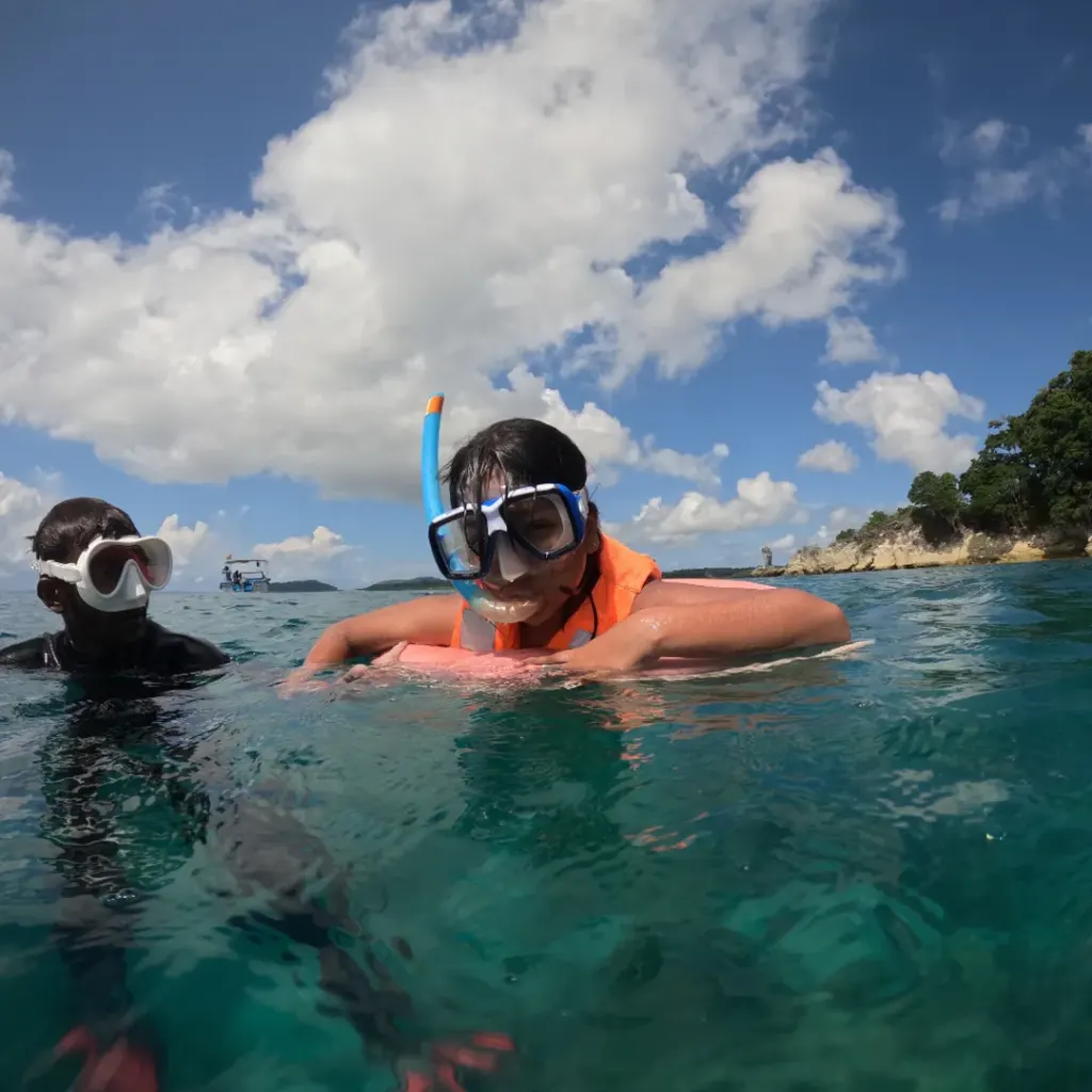 Snorkellers in masks at the surface with an island behind, island hopping in Andaman