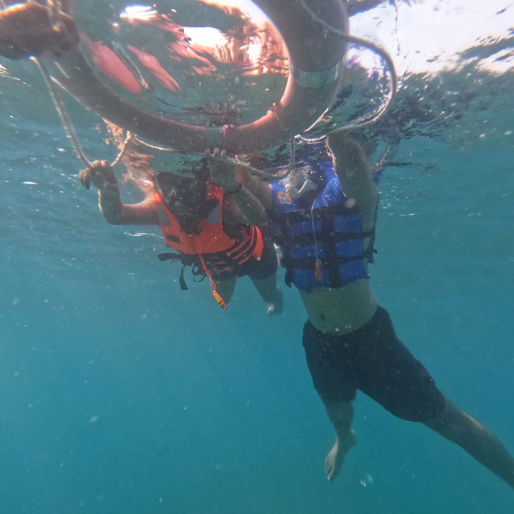 Snorkeller in a blue life jacket under the float ring with another guest in orange behind, seen from below