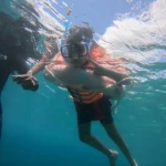 Young snorkeller in a blue mask and orange life jacket resting on the float ring at the surface, Havelock snorkeling