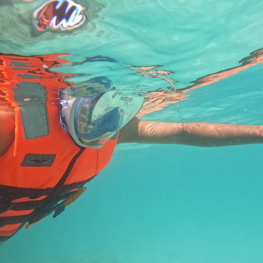 Close-up from below of a snorkeller in a full-face mask and orange life jacket at the surface