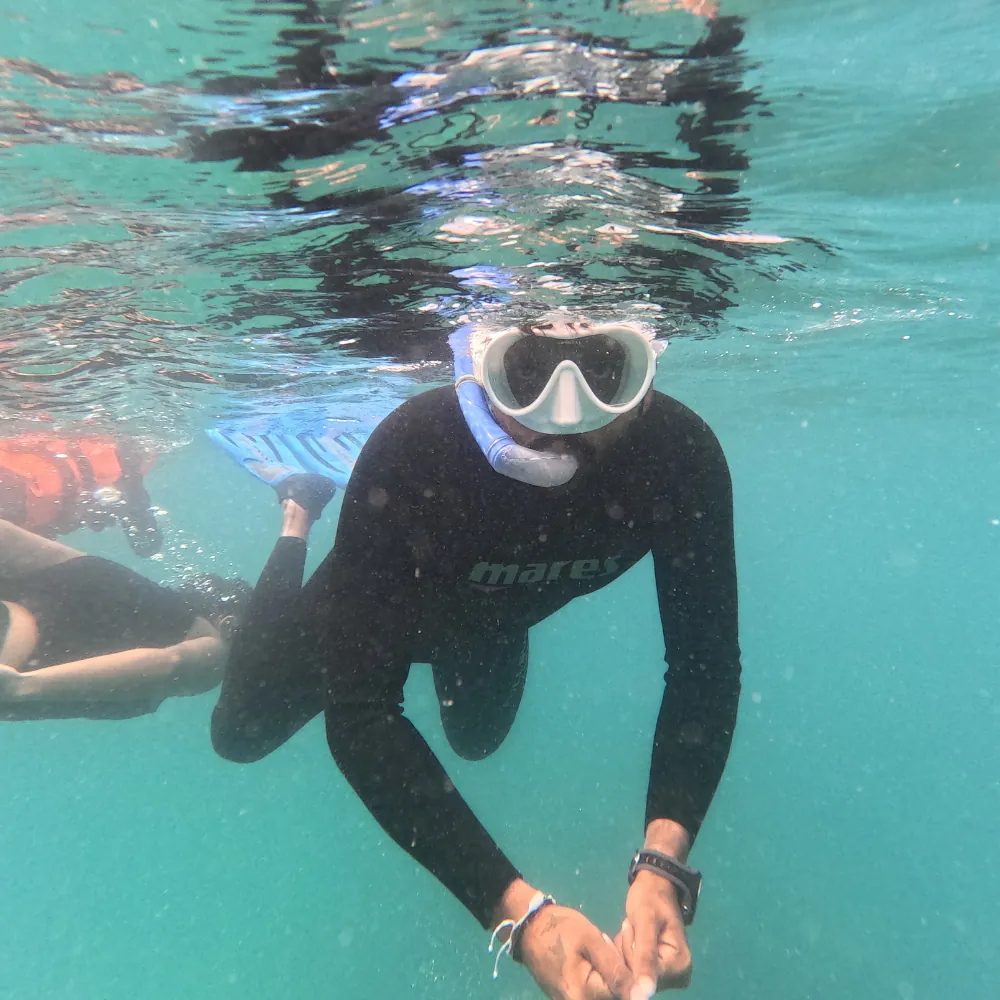 Snorkeller in a black rash guard and white mask with snorkel, hands together, just under the surface