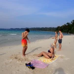 Guests relaxing on a white sand beach by the forest, island hopping in Andaman