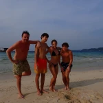 Four friends standing together on a white sand beach, island hopping in Andaman