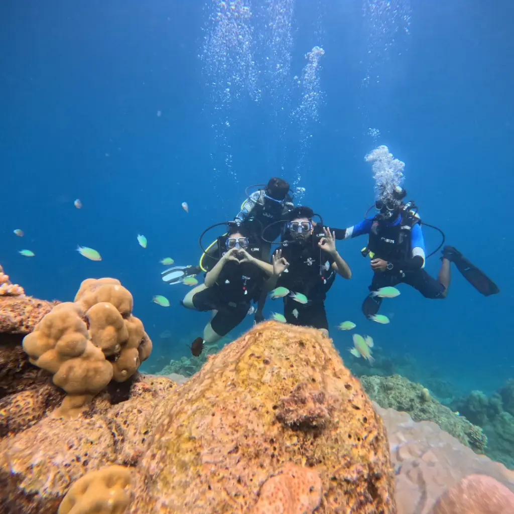 Three divers posing above big potato coral heads in clear blue water, Juvi's scuba diving, Havelock Island