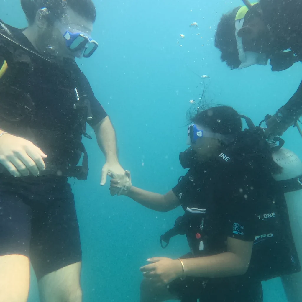 Instructor holding a beginner diver's hand underwater during a scuba dive at Nemo Beach, Havelock
