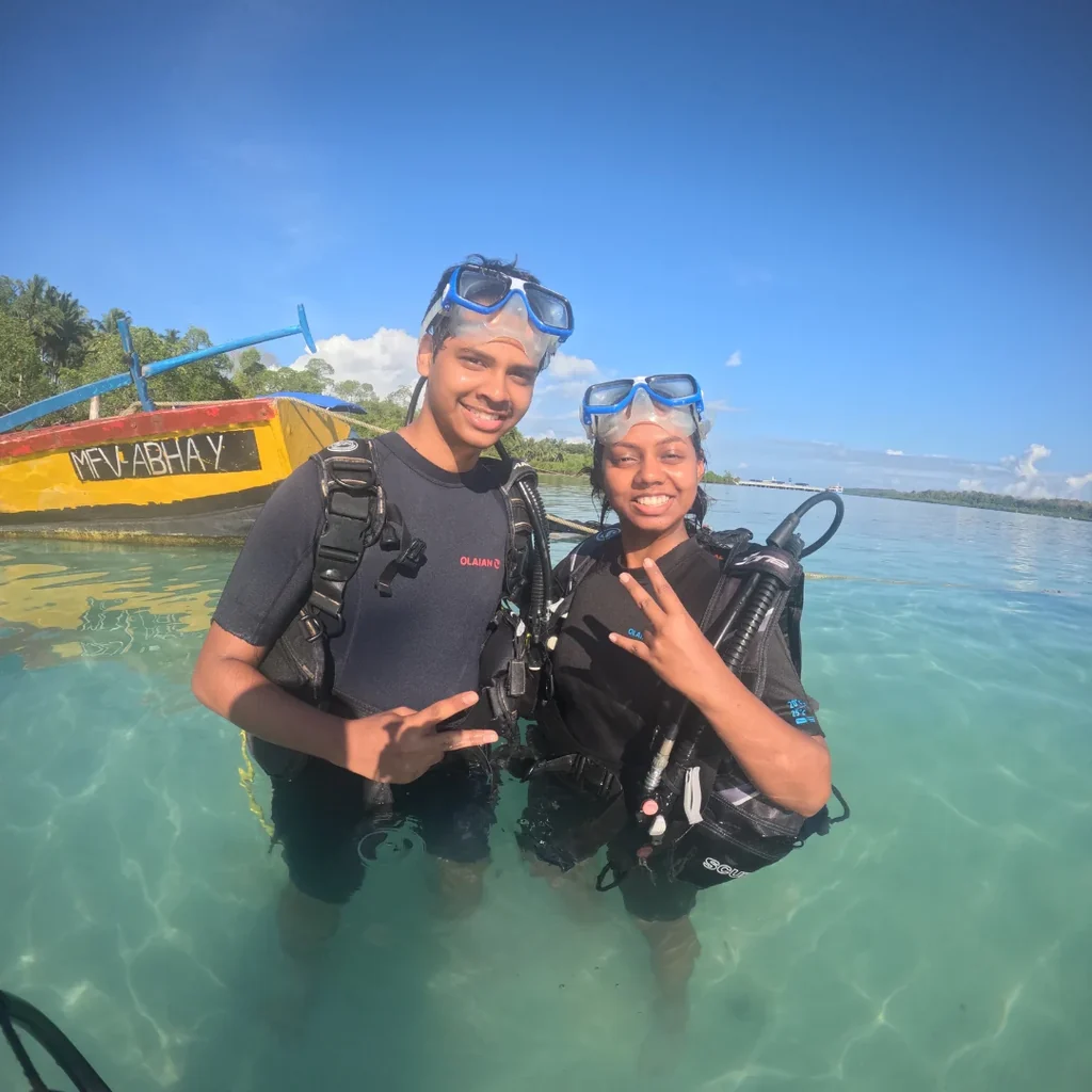 Two divers in scuba gear standing in the shallow water at Nemo Beach, Havelock, before their dive