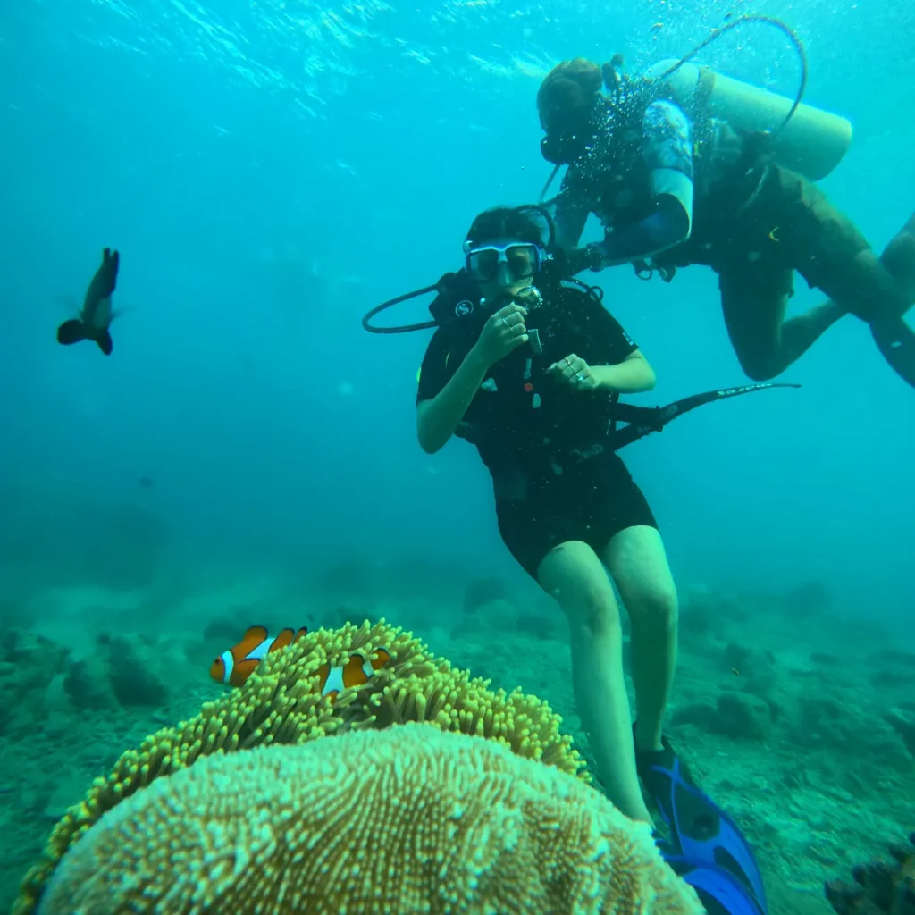 Scuba diver at Nemo Beach, Havelock, hovering above a clownfish anemone with her instructor alongside