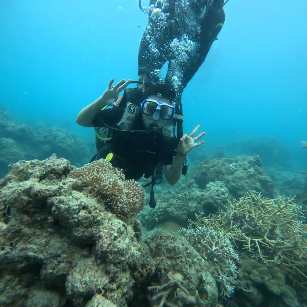 Diver making a hand sign above the coral reef, RAID Advanced 35 course in Havelock, Andaman