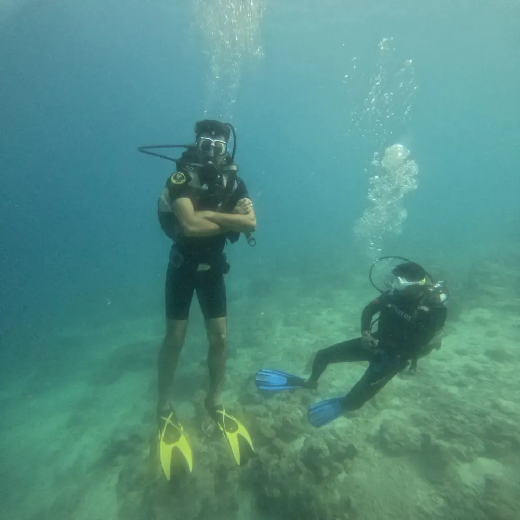 Diver kneeling on the sand with the instructor beside, RAID Open Water course in Havelock, Andaman