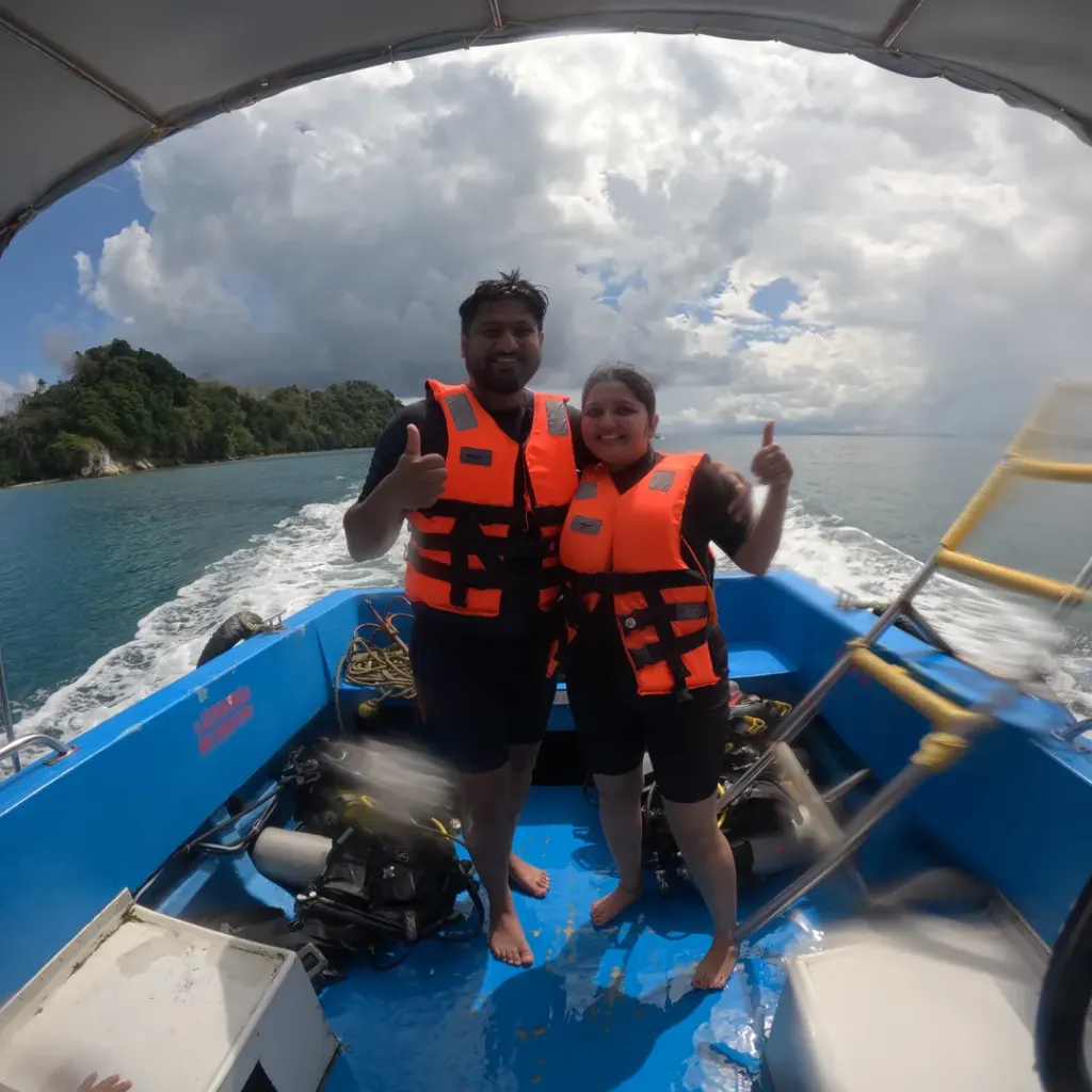 Couple in life jackets on the boat with an island and wake behind, island hopping in Andaman