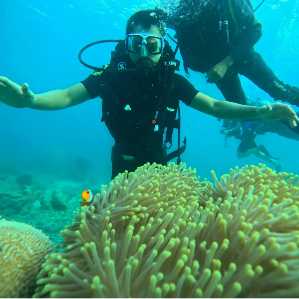 Beginner scuba diving in Nemo Beach, Havelock, with a diver floating above a sea anemone and a single clownfish