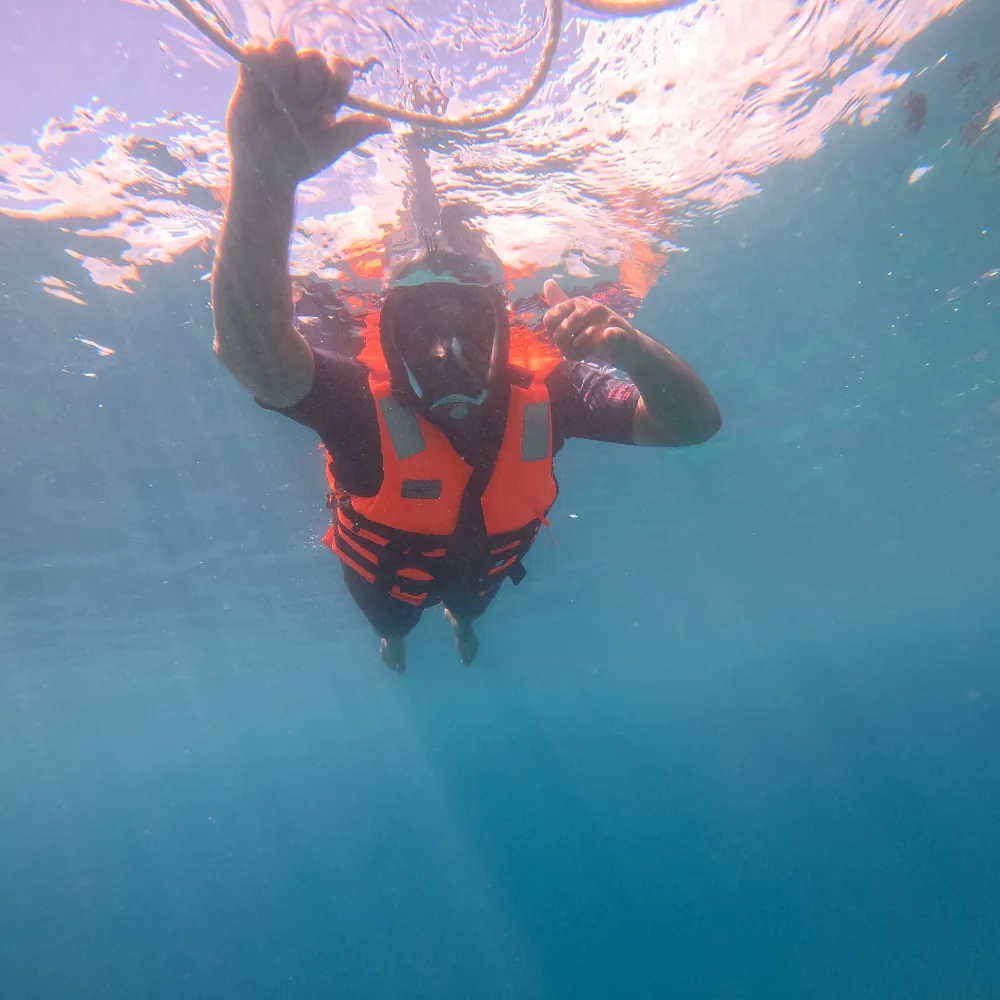 Snorkeller in an orange life jacket holding the float ring rope, seen from below, snorkeling in Havelock Island