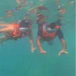 Two snorkellers in orange life jackets floating face down at the surface, photographed from below