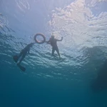 View up from the reef of a snorkeller beside the float ring at the surface and a guide finning below