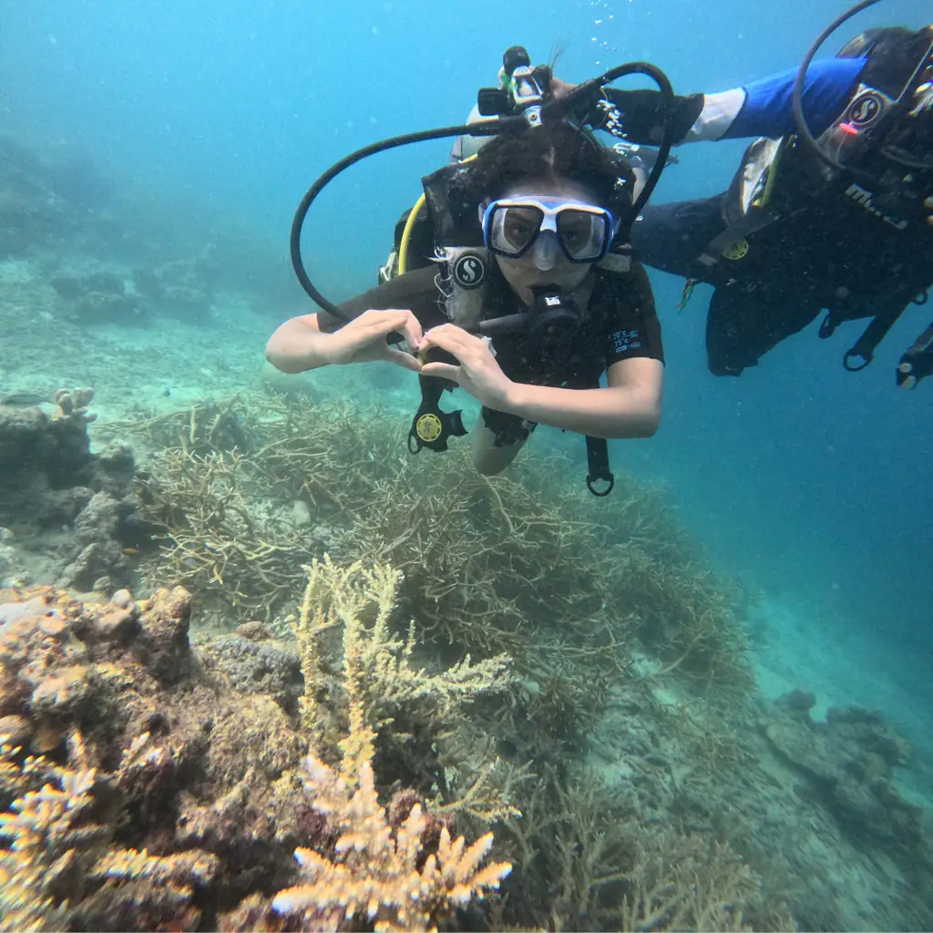 Diver making a heart sign with her hands over the coral field while scuba diving at Tribe Gate, Havelock