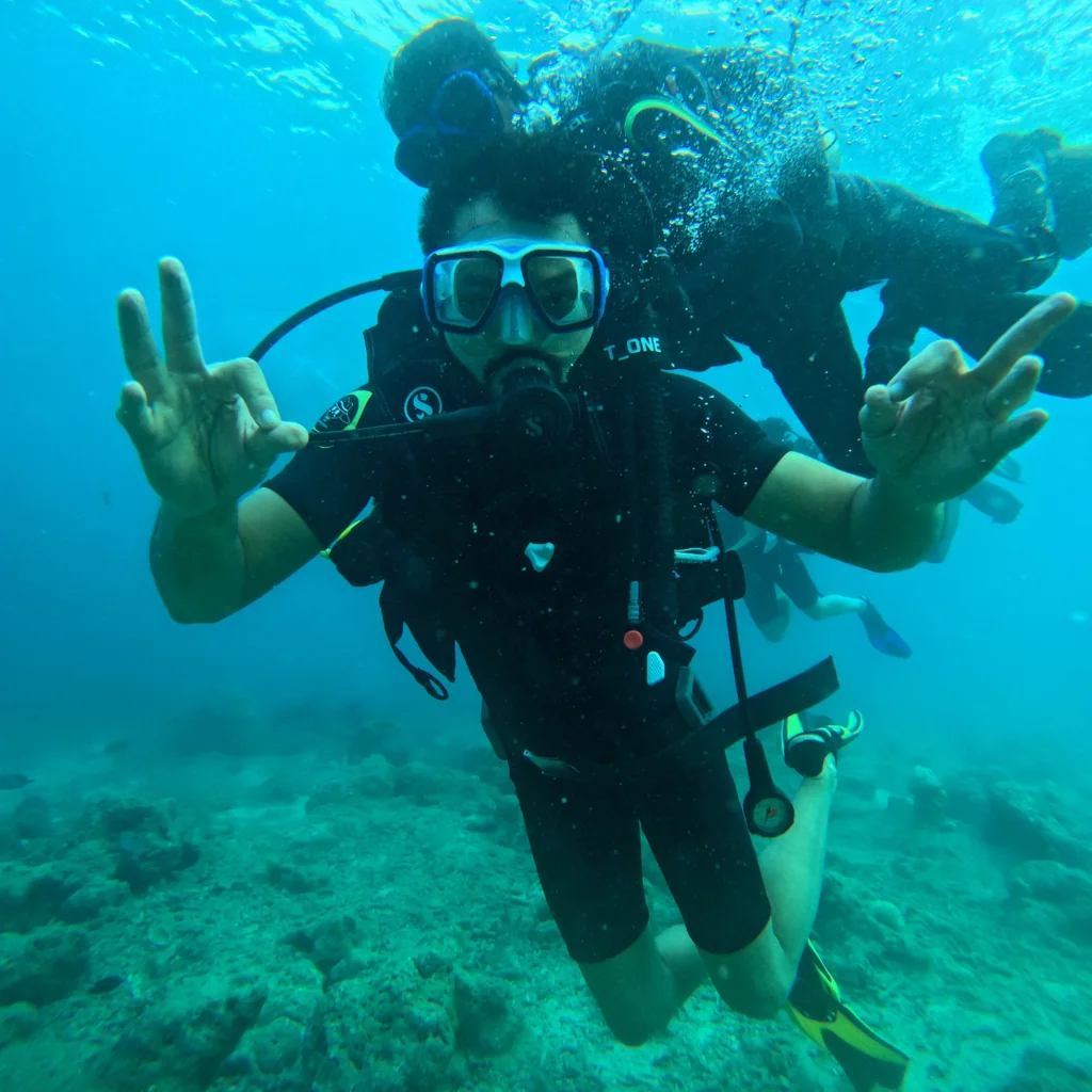 Diver giving a peace sign underwater while scuba diving at Tribe Gate, Havelock Island