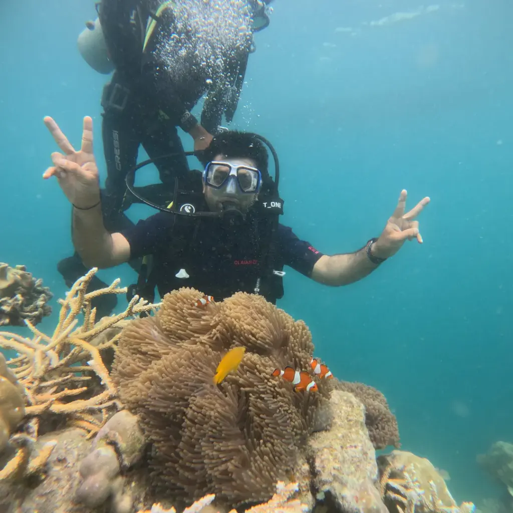 Diver making peace signs above an anemone with clownfish, Try Scuba diving in Havelock Island