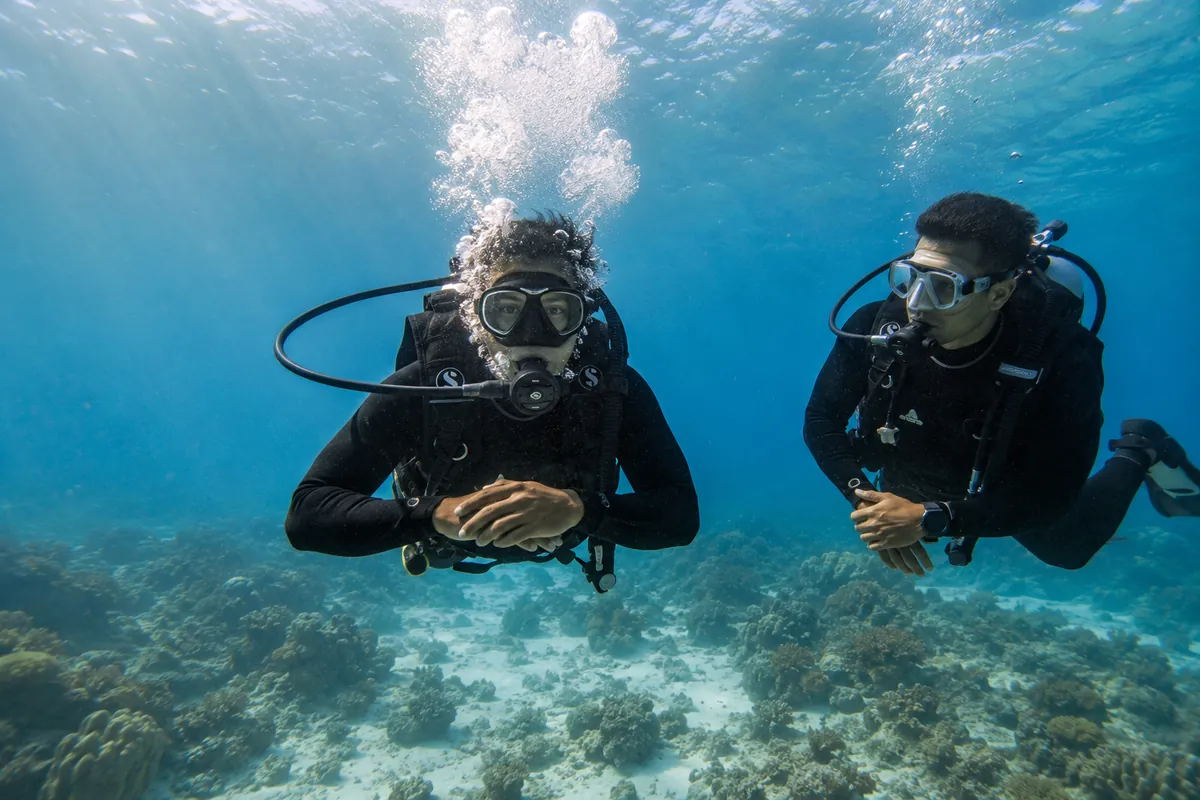 Two divers hovering calmly and exhaling slowly over the reef