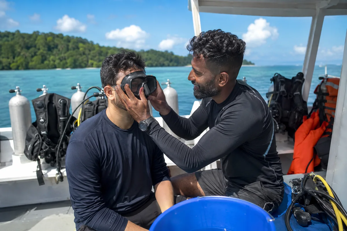 Instructor checking a beginner's mask fit on the dive boat before a scuba dive