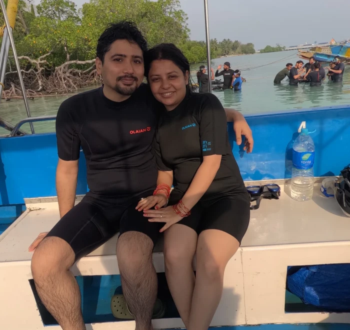 Couple in wetsuits sitting on the dive boat with the mangroves behind