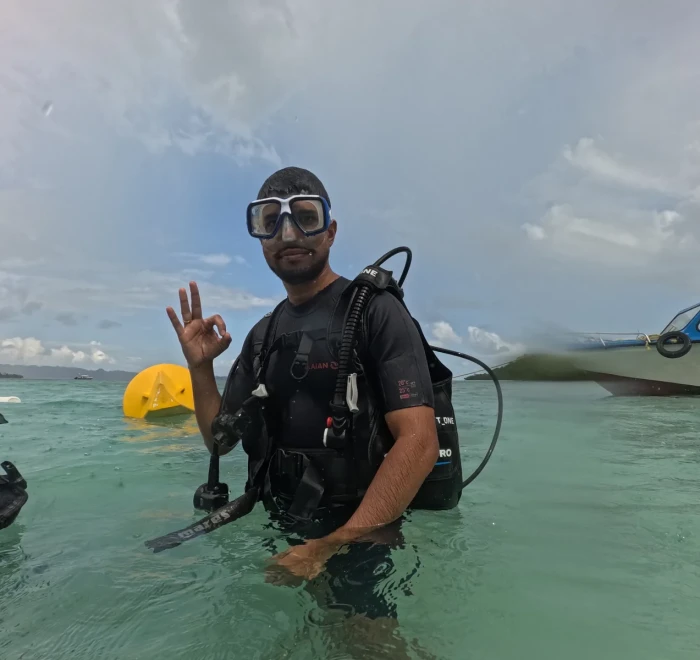 Diver giving the OK sign in the shallows with the boat behind