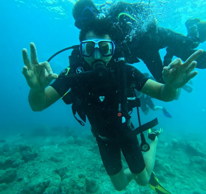 Diver giving OK signals with both hands in the shallow water of a reef