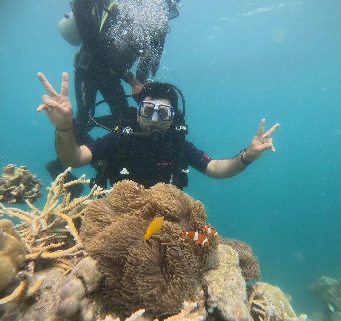 Diver giving peace signs beside a clownfish anemone