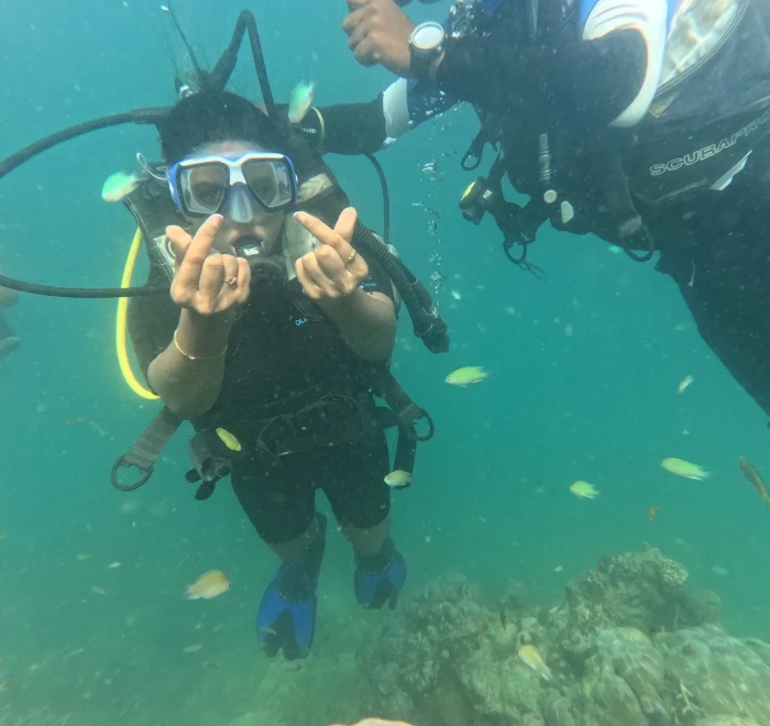 Diver giving peace signs with reef fish all around while diving in Havelock Island