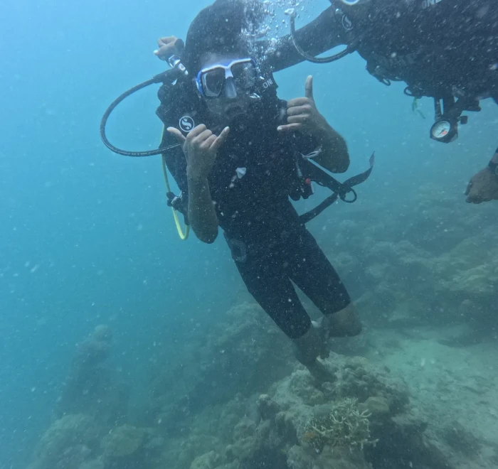 Diver giving a thumbs up over the sandy patch beside the reef