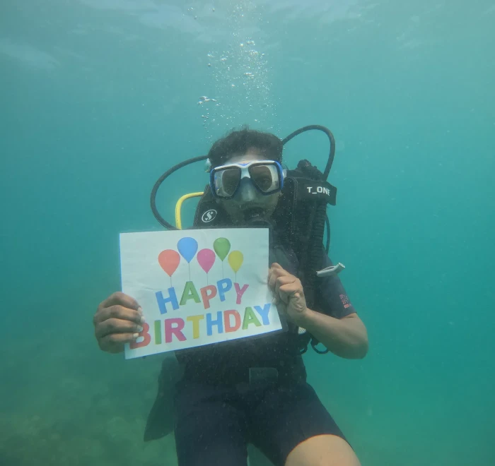 Diver holding a happy birthday sign underwater on a celebration dive