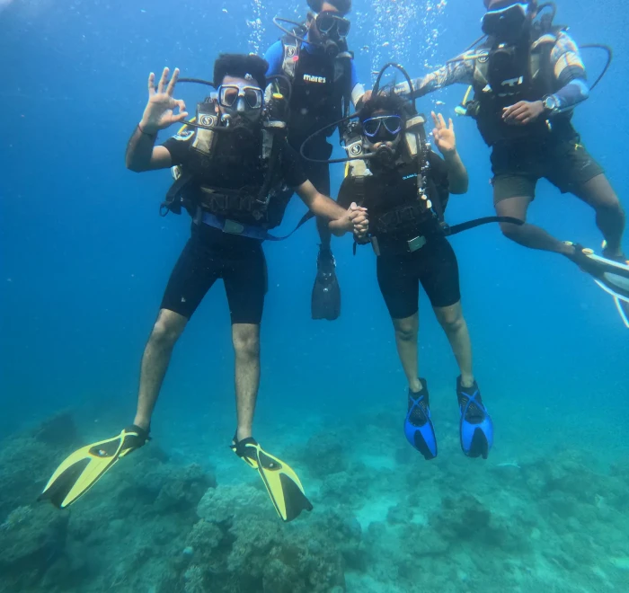 Group of four divers giving the OK signal over the reef in clear blue water