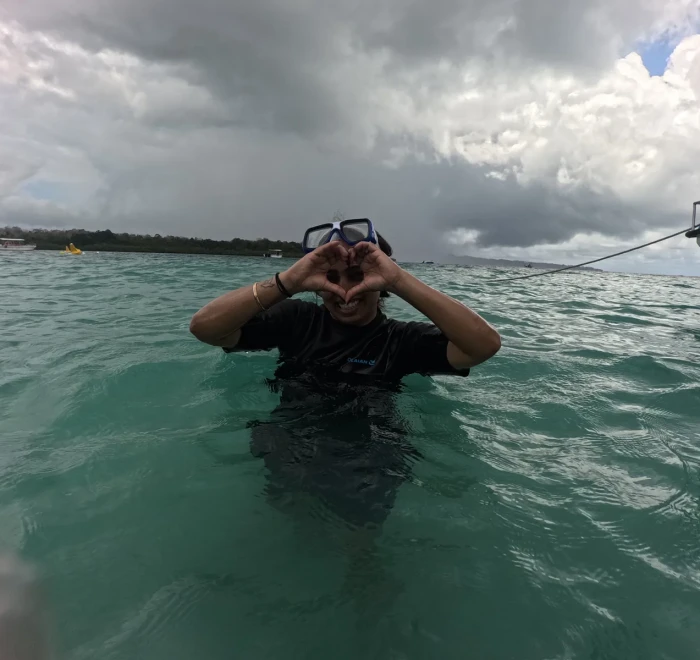 Guest making a heart shape in the shallows with the boat behind