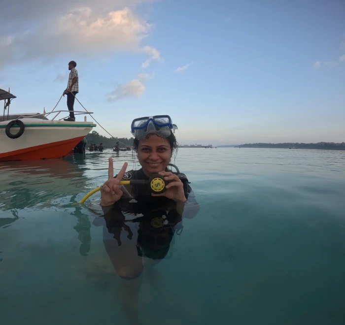 Guest in the shallows at sunset with the dive boat behind