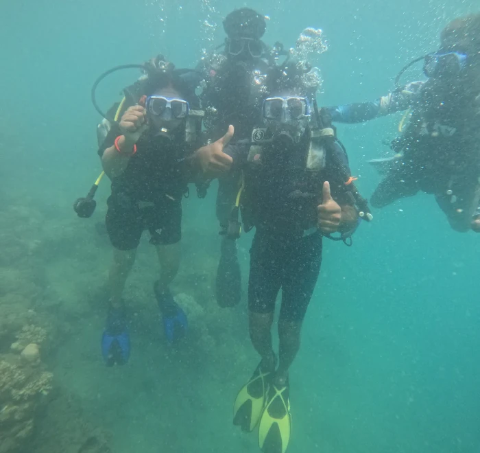 Three divers giving thumbs up together underwater