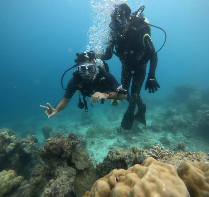 Two divers above the coral, one giving a peace sign