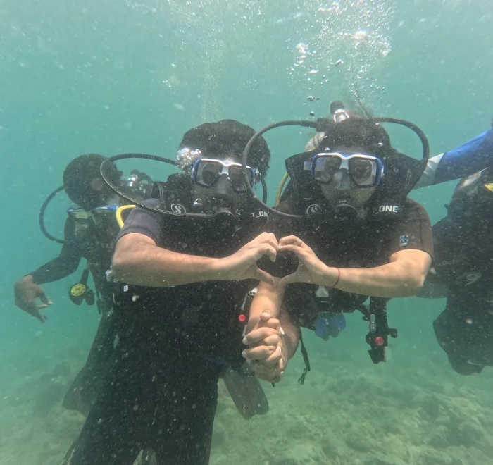 Two divers making a heart shape underwater with the group behind