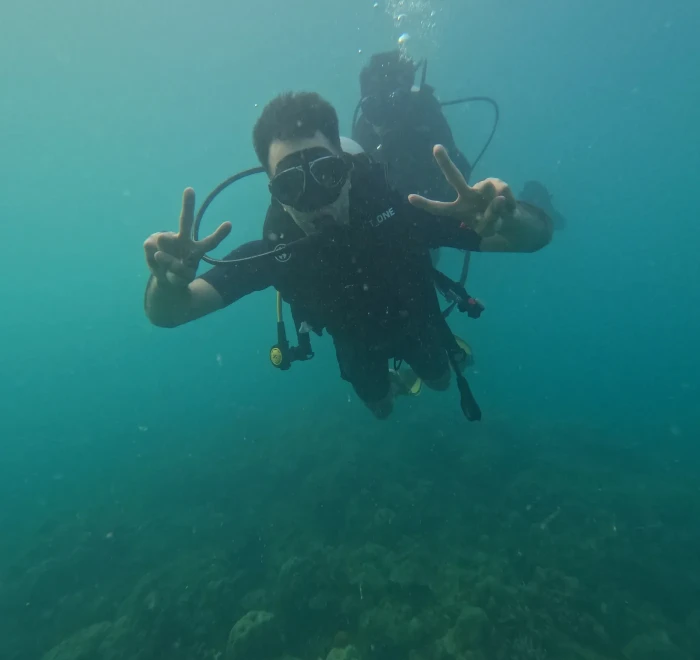 Two divers underwater, one giving a peace sign to the camera