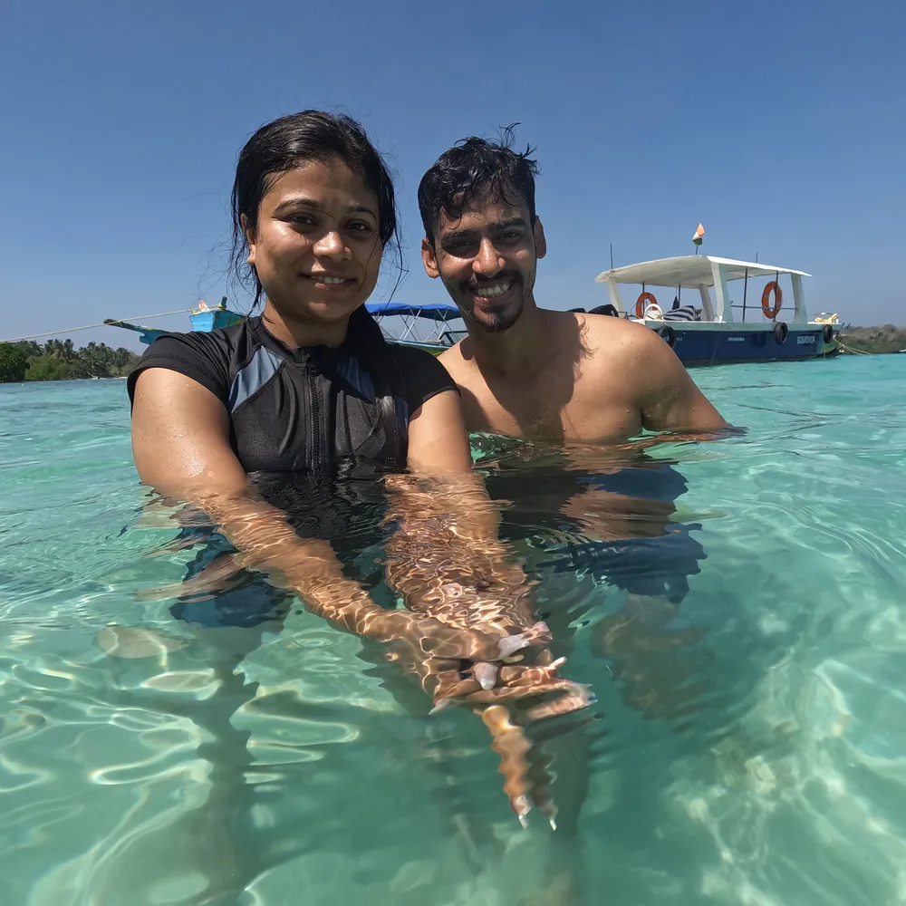Couple standing in clear shallow water beside the Frogman boat on a Cinque Island day trip, Andaman