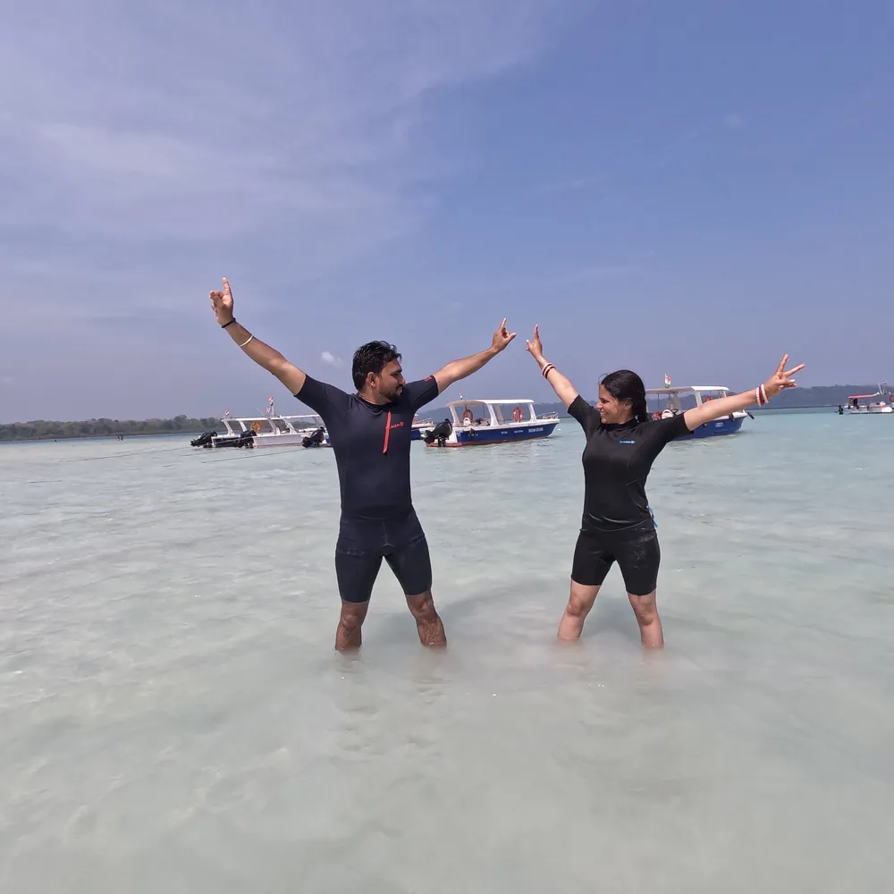 Two guests on the sandbar at Cinque Island with the boat anchored behind, Andaman
