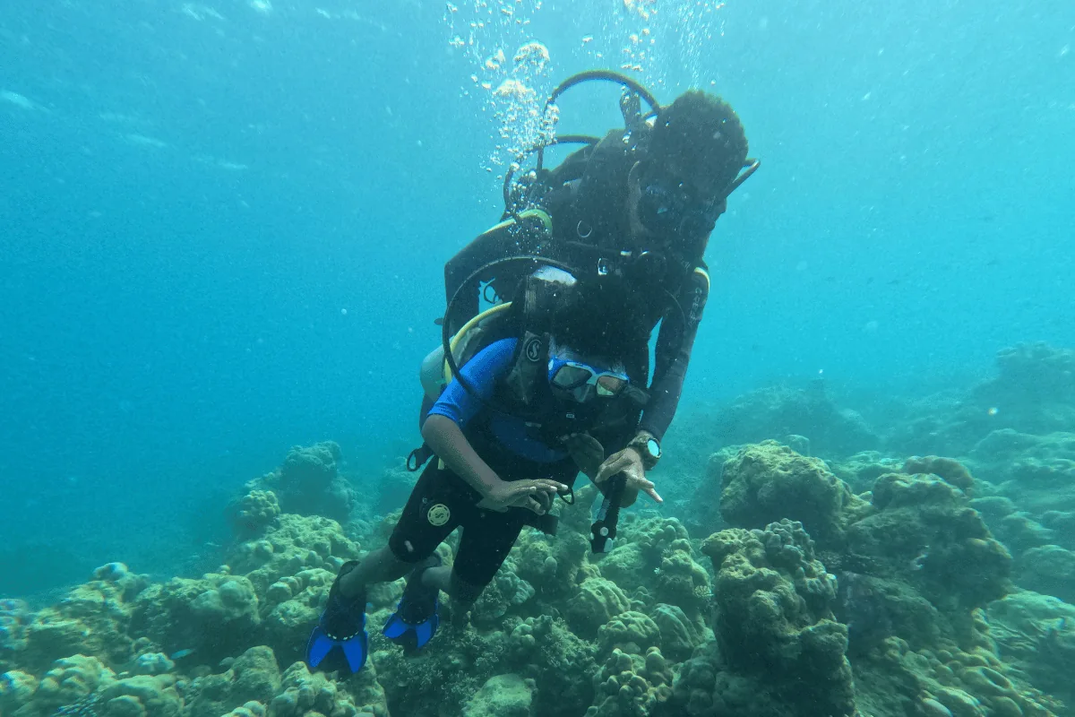 Instructor holding a young diver close on a slow, shallow descent over coral reef in Havelock, Andaman