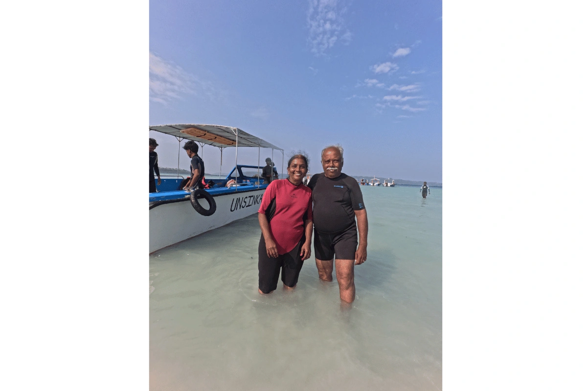 Two older guests in wetsuits smiling in shallow water beside the dive boat before scuba diving in Havelock, Andaman